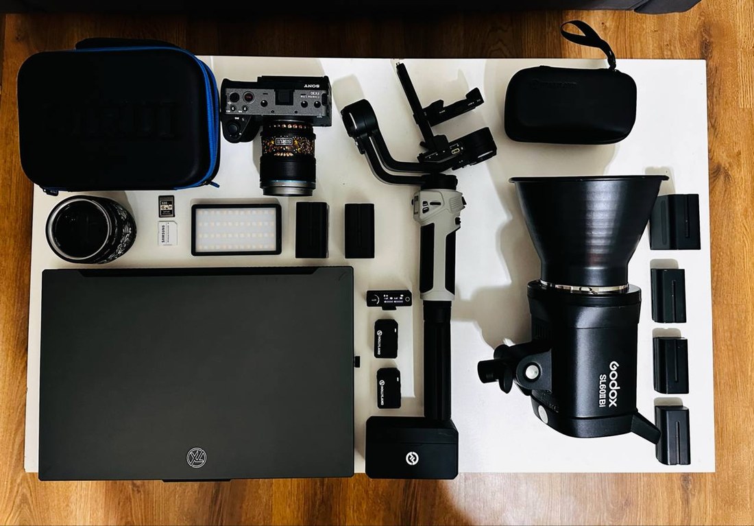Разложенная на столе съёмочная техника: камера Sony, объективы, свет Godox, стедикам, петличные микрофоны, ноутбук, батареи
